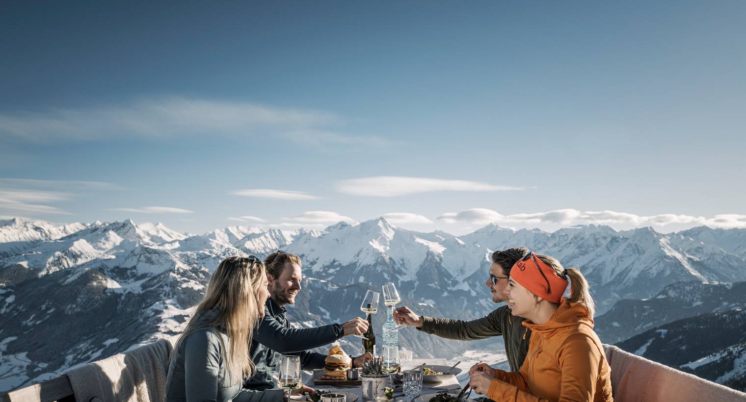Eine Gruppe an Freunden haben eine geselliges Essen auf der Kistallhütte mit schneebedeckten Bergen