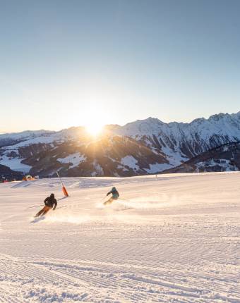 Skifahrer fahren entlang einer Piste im Hintergrund geht die Sonne auf