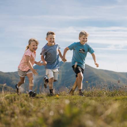 Kinder rennen über eine Almwiese und haben ein Lachen im Gesicht
