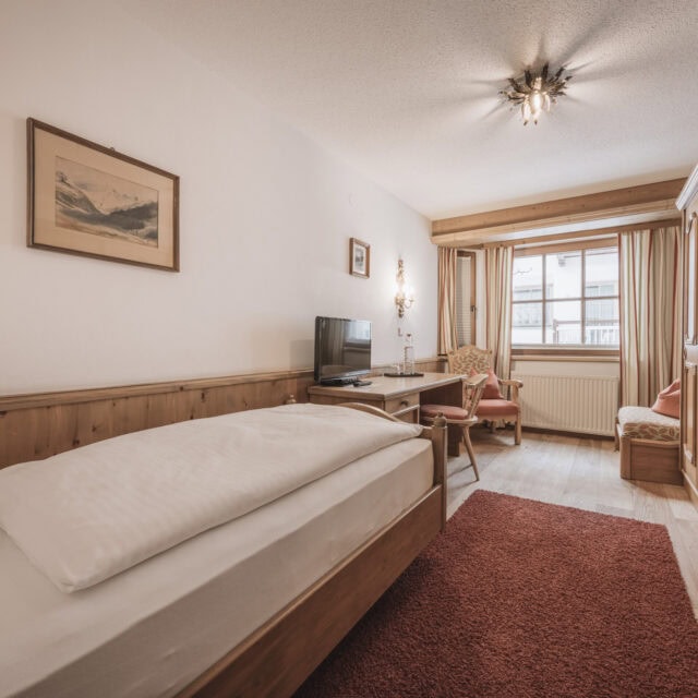 einzelzimmer auerberg2 Gemütliches Schlafzimmer mit Holzdetails und Fernseher.