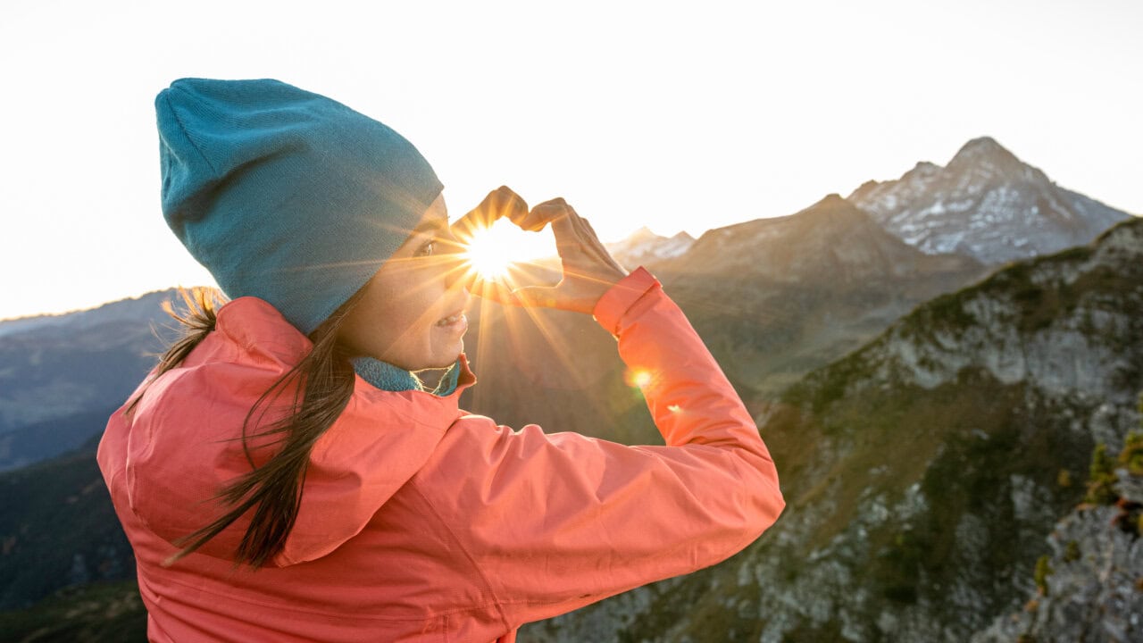 Frau formt Herz mit Händen gegen Sonnenaufgang.