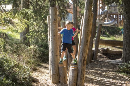 Kinder spielen und balancieren auf Holzstämmen.