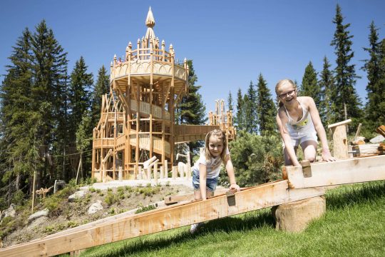 Kinder spielen auf einem Holzspielplatz im Freien.