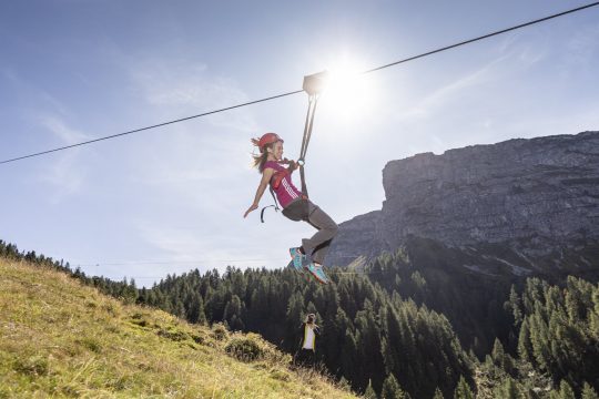 Frau fährt mit Zipline über Berglandschaft.
