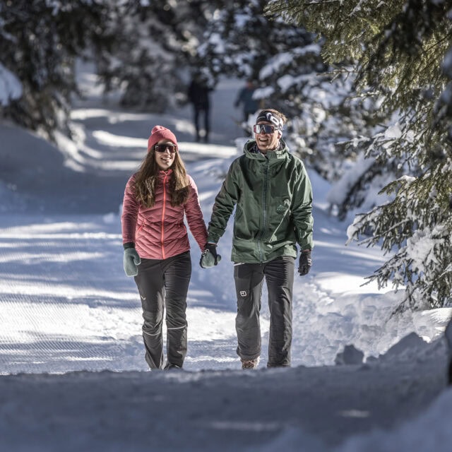 zillertalarena 05 winterwandern Paar spaziert im Schnee unter Bäumen.