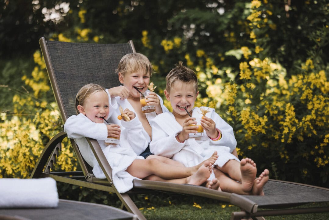 Drei Kinder in Bademänteln genießen Getränke im Garten.