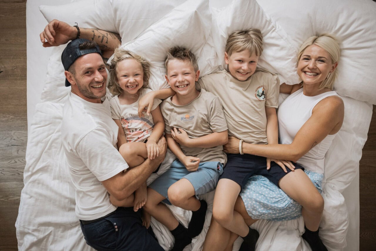 Familie posiert glücklich auf einem Bett.